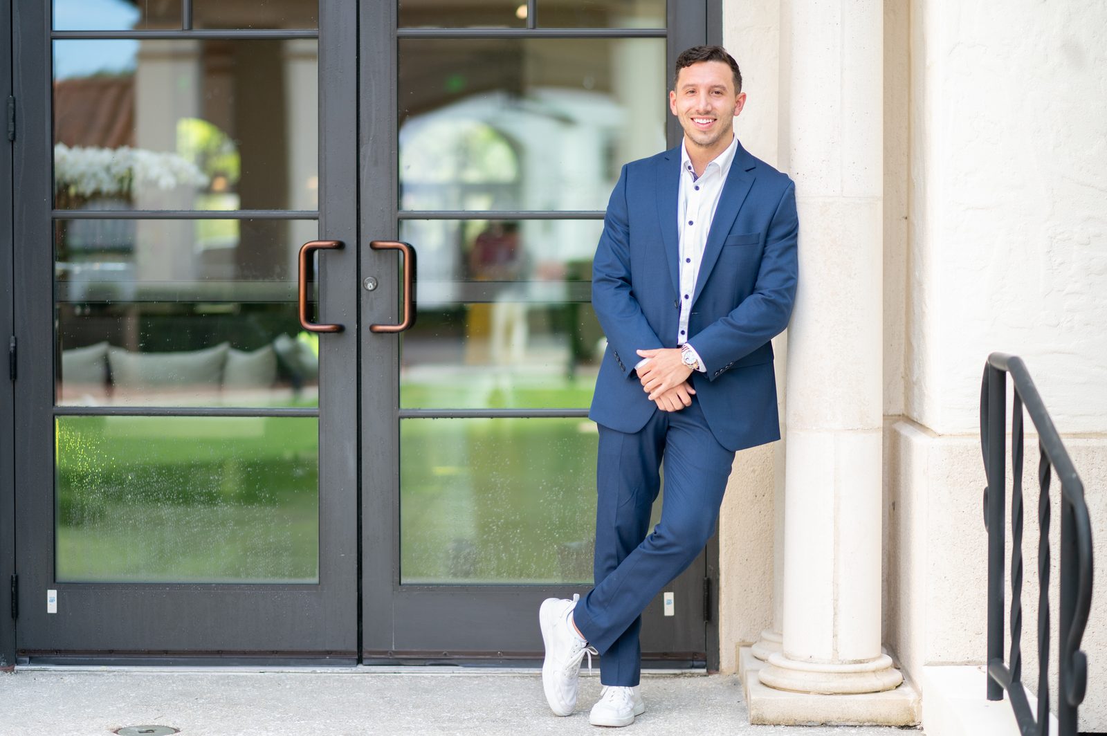 Tony Ubaldini in a blue suit leaning on a column by glass doors